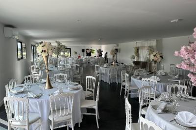 Salle de réception lumineuse avec tables rondes décorées de nappes blanches, fleurs et vaisselle élégante.