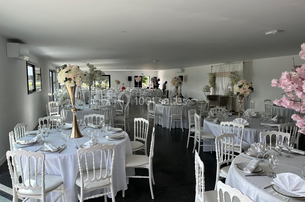 Salle de réception élégamment décorée avec des tables rondes, nappes blanches et centres de table fleuris.