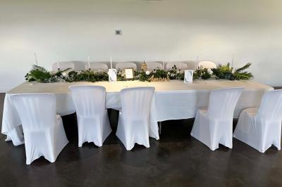 Salle de réception lumineuse avec tables rondes décorées de nappes blanches, fleurs et vaisselle élégante.