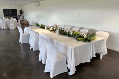 Salle de réception lumineuse avec tables rondes décorées de nappes blanches, fleurs et vaisselle élégante.