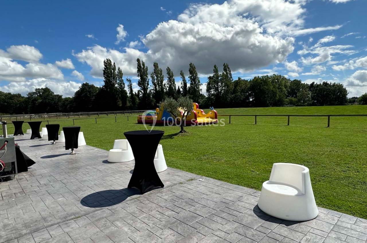 Espace extérieur avec pelouse, tables hautes noires, fauteuils blancs et structure gonflable colorée en arrière-plan.