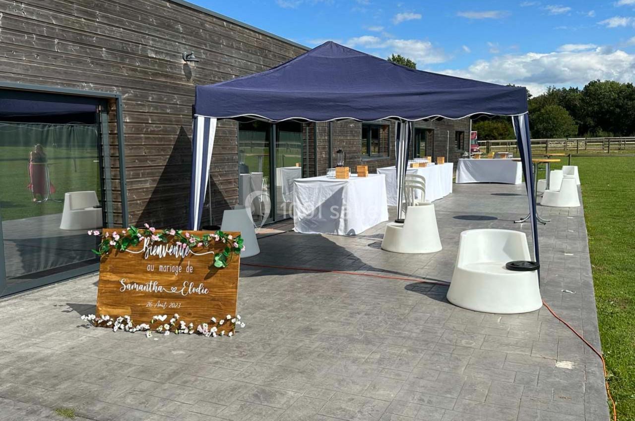 Panneau de bienvenue en bois devant une tente avec tables dressées sur une terrasse en plein air.