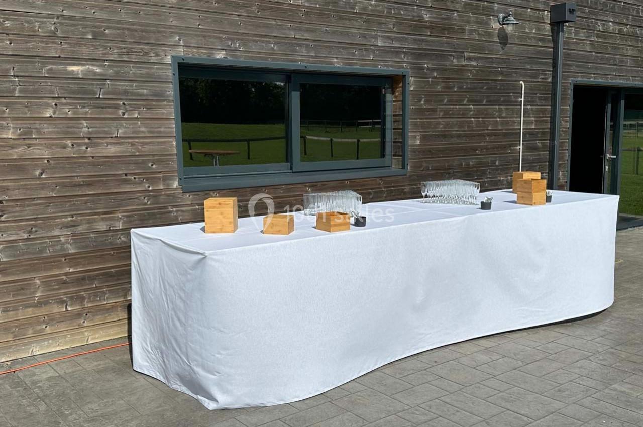 Table drapée de blanc avec des verres et des boîtes en bois, placée devant un mur en bois et une fenêtre.