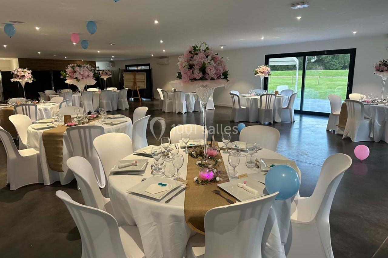 Salle de réception décorée avec des tables rondes, nappes blanches, centres de table fleuris et ballons colorés.