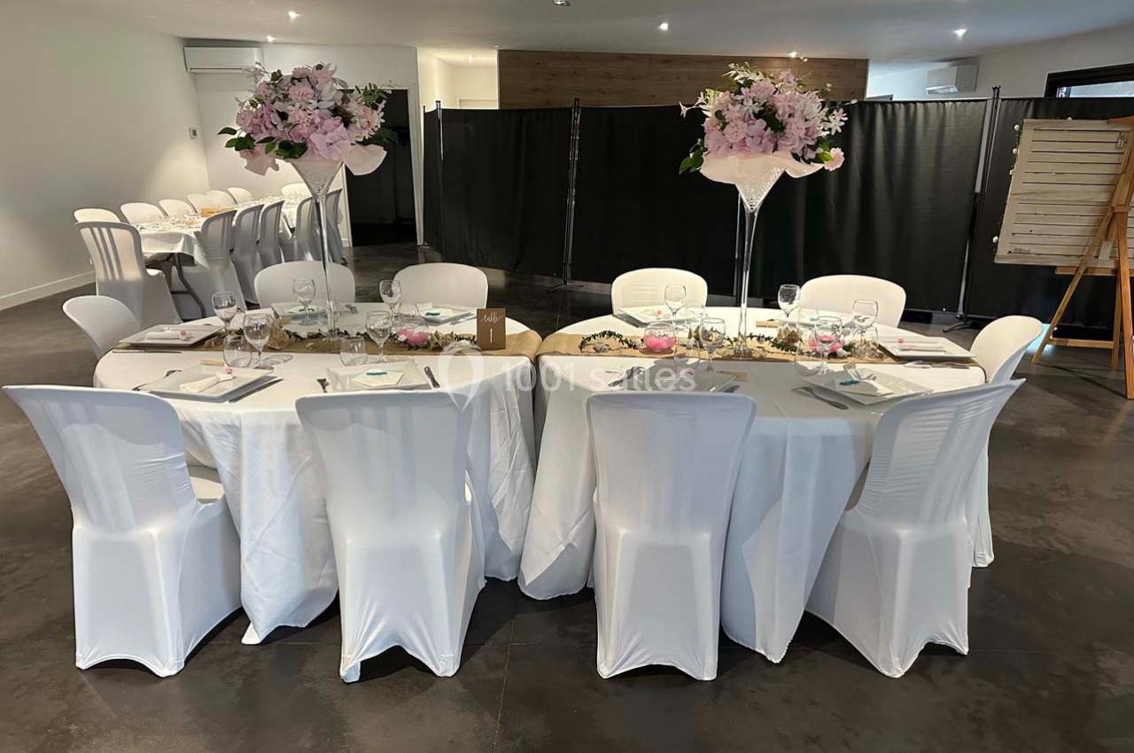 Tables rondes décorées avec nappes blanches, chaises assorties et centres de table fleuris dans une salle de réception.