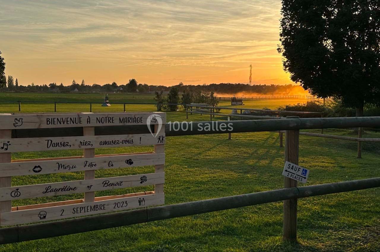Panneau en bois annonçant un mariage, installé dans un champ au coucher du soleil avec une clôture en bois.