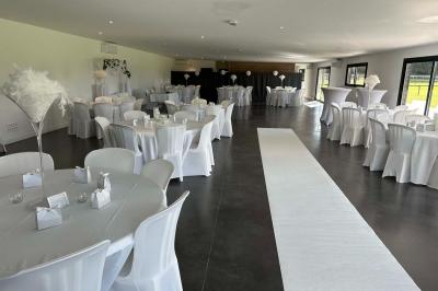 Salle de réception lumineuse avec tables rondes décorées de nappes blanches, fleurs et vaisselle élégante.