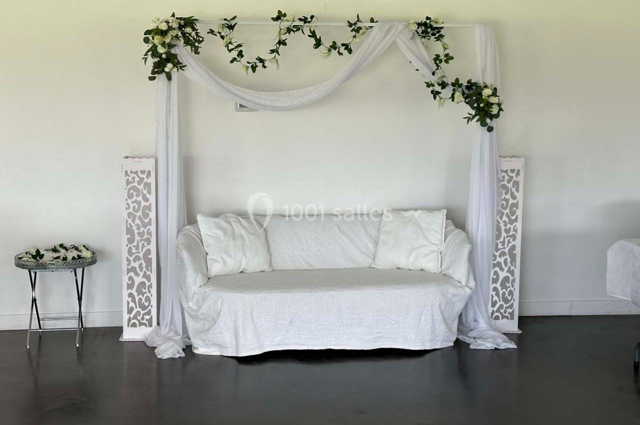 Canapé blanc décoré de drapés et de feuillages, encadré par deux colonnes ajourées dans une pièce lumineuse.