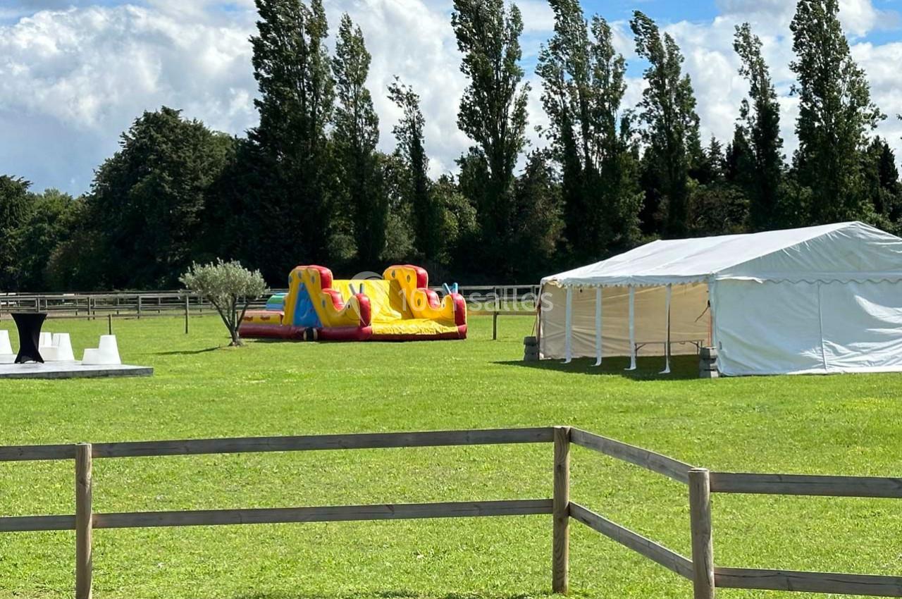 Structure gonflable colorée et tente blanche installées sur une pelouse entourée d'arbres et de clôtures en bois.