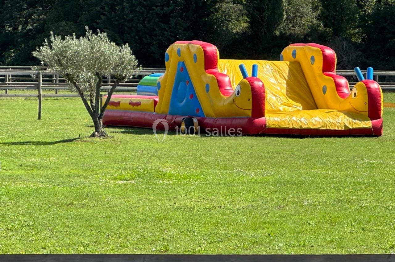 Structure gonflable colorée en forme d'escargots sur une pelouse, avec un arbre et une clôture en arrière-plan.