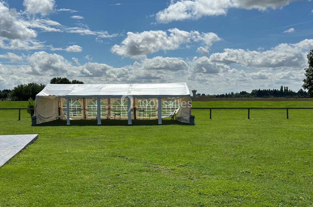 Tente blanche installée sur une pelouse verte sous un ciel partiellement nuageux.