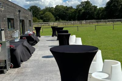 Salle de réception lumineuse avec tables rondes décorées de nappes blanches, fleurs et vaisselle élégante.