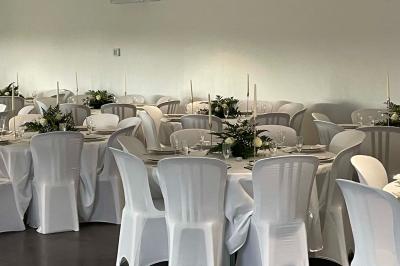 Salle de réception lumineuse avec tables rondes décorées de nappes blanches, fleurs et vaisselle élégante.