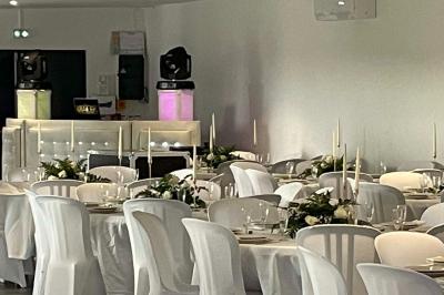 Salle de réception lumineuse avec tables rondes décorées de nappes blanches, fleurs et vaisselle élégante.