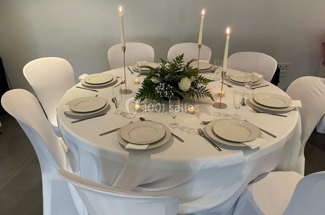 Table ronde élégamment dressée avec nappes blanches, bougies allumées, vaisselle et centre de table floral.