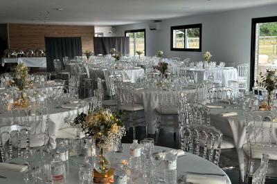 Salle de réception lumineuse avec tables rondes décorées de nappes blanches, fleurs et vaisselle élégante.
