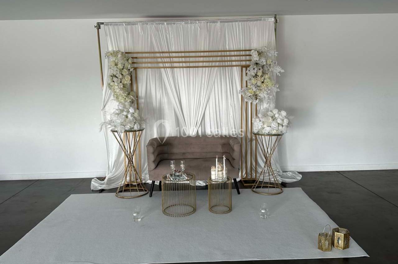 Décor minimaliste avec un canapé beige devant un rideau blanc, entouré de fleurs blanches et de tables dorées.