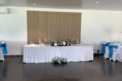 Salle de réception lumineuse avec tables rondes décorées de nappes blanches, fleurs et vaisselle élégante.