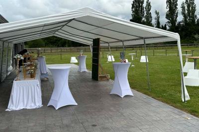 Salle de réception lumineuse avec tables rondes décorées de nappes blanches, fleurs et vaisselle élégante.