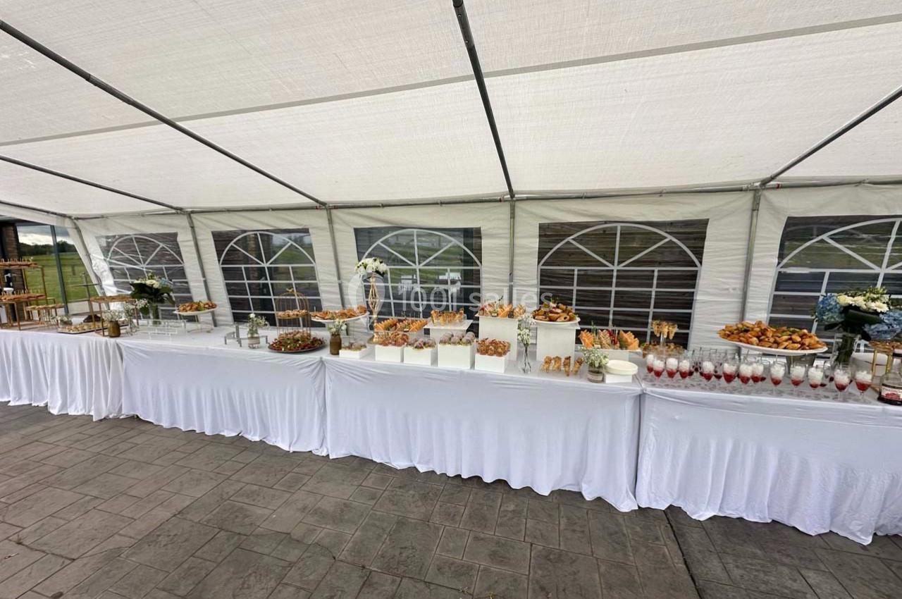 Buffet varié disposé sous une tente blanche, avec des plats salés et sucrés présentés sur des nappes blanches.