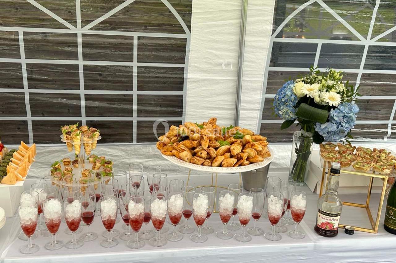 Buffet avec viennoiseries, verrines, fleurs et boissons servies dans des flûtes sur une table décorée sous une tente blanche.