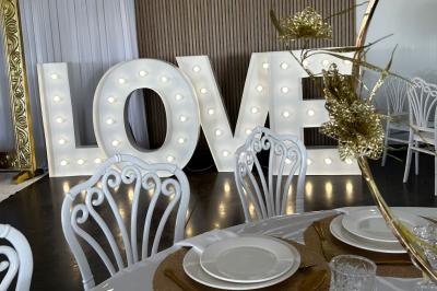 Salle de réception lumineuse avec tables rondes décorées de nappes blanches, fleurs et vaisselle élégante.