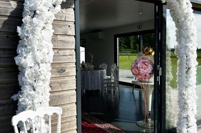 Salle de réception lumineuse avec tables rondes décorées de nappes blanches, fleurs et vaisselle élégante.