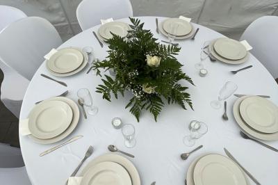 Salle de réception lumineuse avec tables rondes décorées de nappes blanches, fleurs et vaisselle élégante.