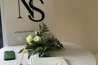 Salle de réception lumineuse avec tables rondes décorées de nappes blanches, fleurs et vaisselle élégante.