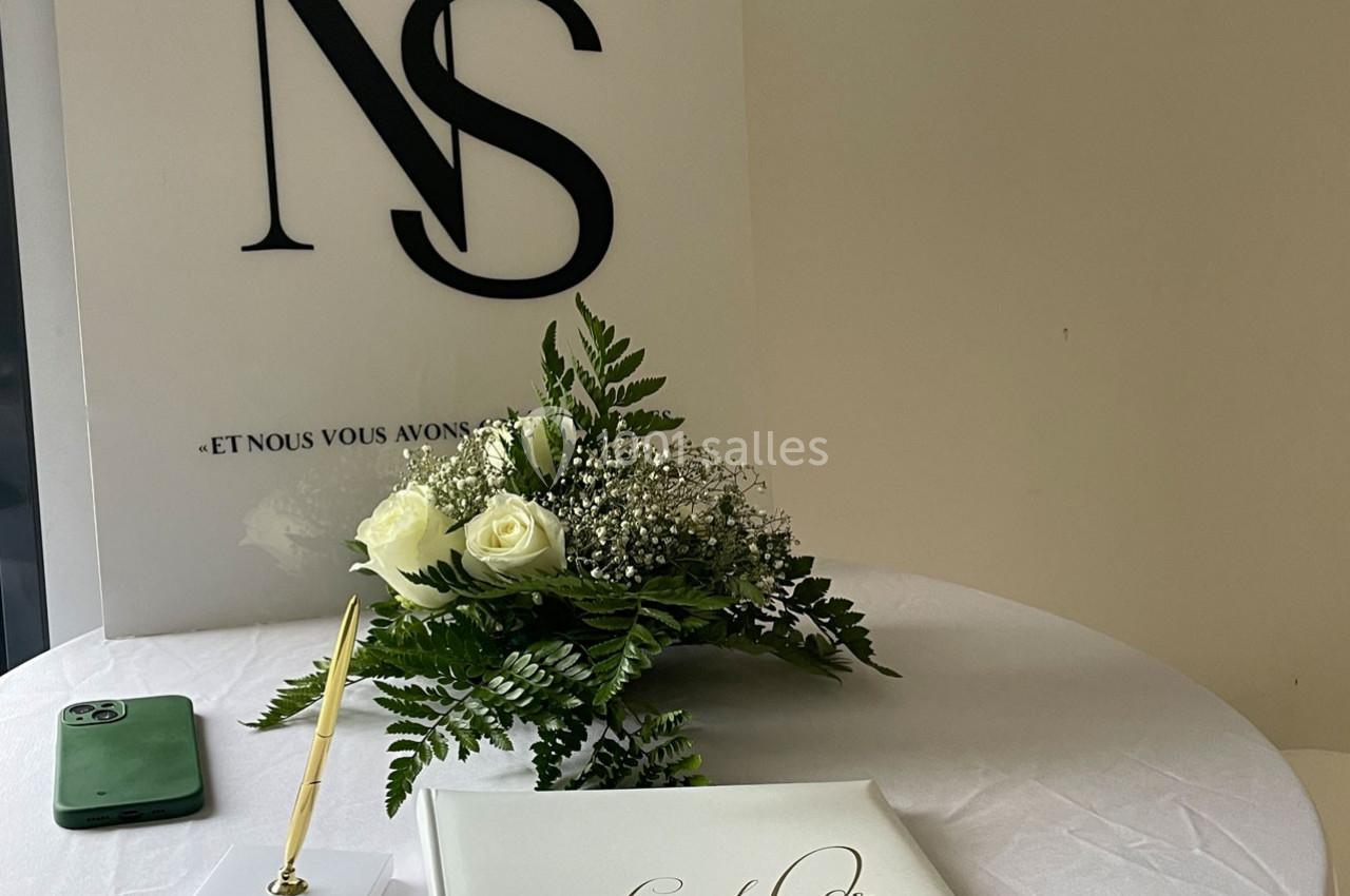 Bouquet de fleurs blanches, livre d'or, stylo doré et smartphone sur une table ronde blanche.