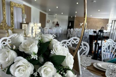 Salle de réception lumineuse avec tables rondes décorées de nappes blanches, fleurs et vaisselle élégante.