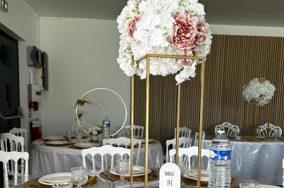 Salle de réception lumineuse avec tables rondes décorées de nappes blanches, fleurs et vaisselle élégante.