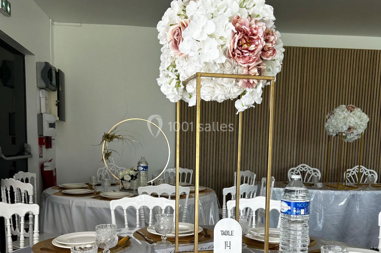 Centre de table floral avec des fleurs blanches et roses sur une structure dorée, entouré de vaisselle élégante.