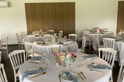 Salle de réception lumineuse avec tables rondes décorées de nappes blanches, fleurs et vaisselle élégante.
