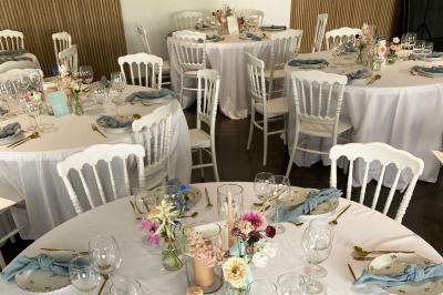 Salle de réception lumineuse avec tables rondes décorées de nappes blanches, fleurs et vaisselle élégante.