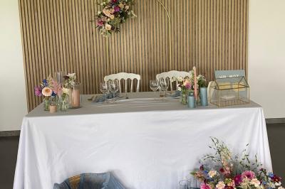 Salle de réception lumineuse avec tables rondes décorées de nappes blanches, fleurs et vaisselle élégante.