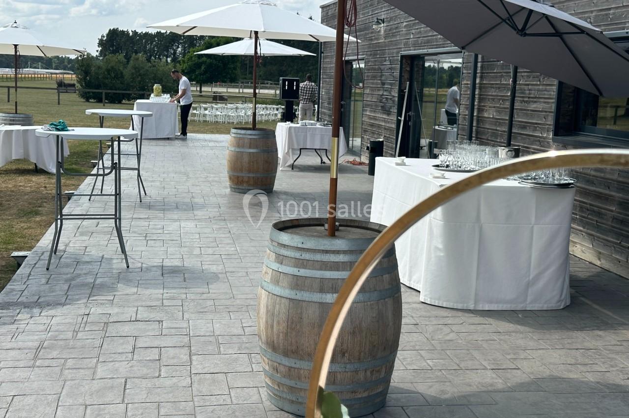 Terrasse extérieure avec tables dressées, parasols et tonneaux en bois, prête pour un événement en plein air.