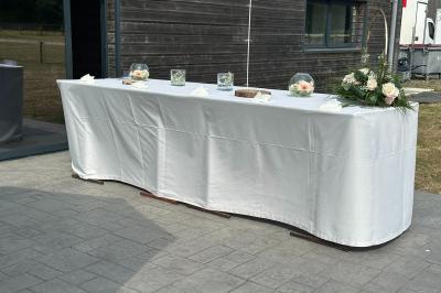 Salle de réception lumineuse avec tables rondes décorées de nappes blanches, fleurs et vaisselle élégante.