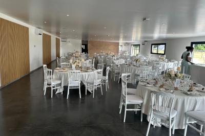 Salle de réception lumineuse avec tables rondes décorées de nappes blanches, fleurs et vaisselle élégante.