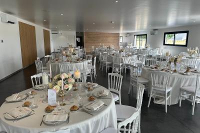 Salle de réception lumineuse avec tables rondes décorées de nappes blanches, fleurs et vaisselle élégante.