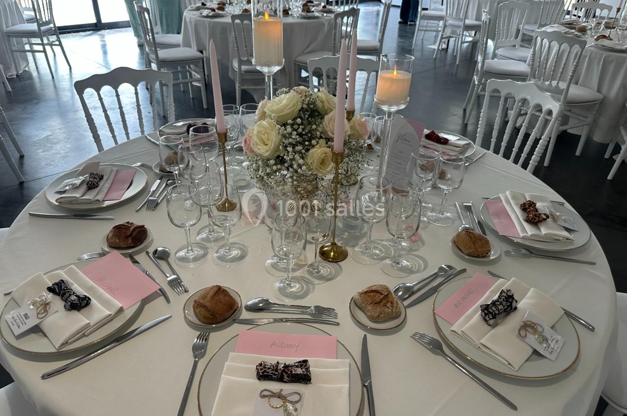 Table de réception élégamment dressée avec nappes blanches, bougies, fleurs et couverts disposés pour un repas formel.