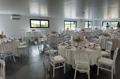 Salle de réception lumineuse avec tables rondes décorées de nappes blanches, fleurs et vaisselle élégante.
