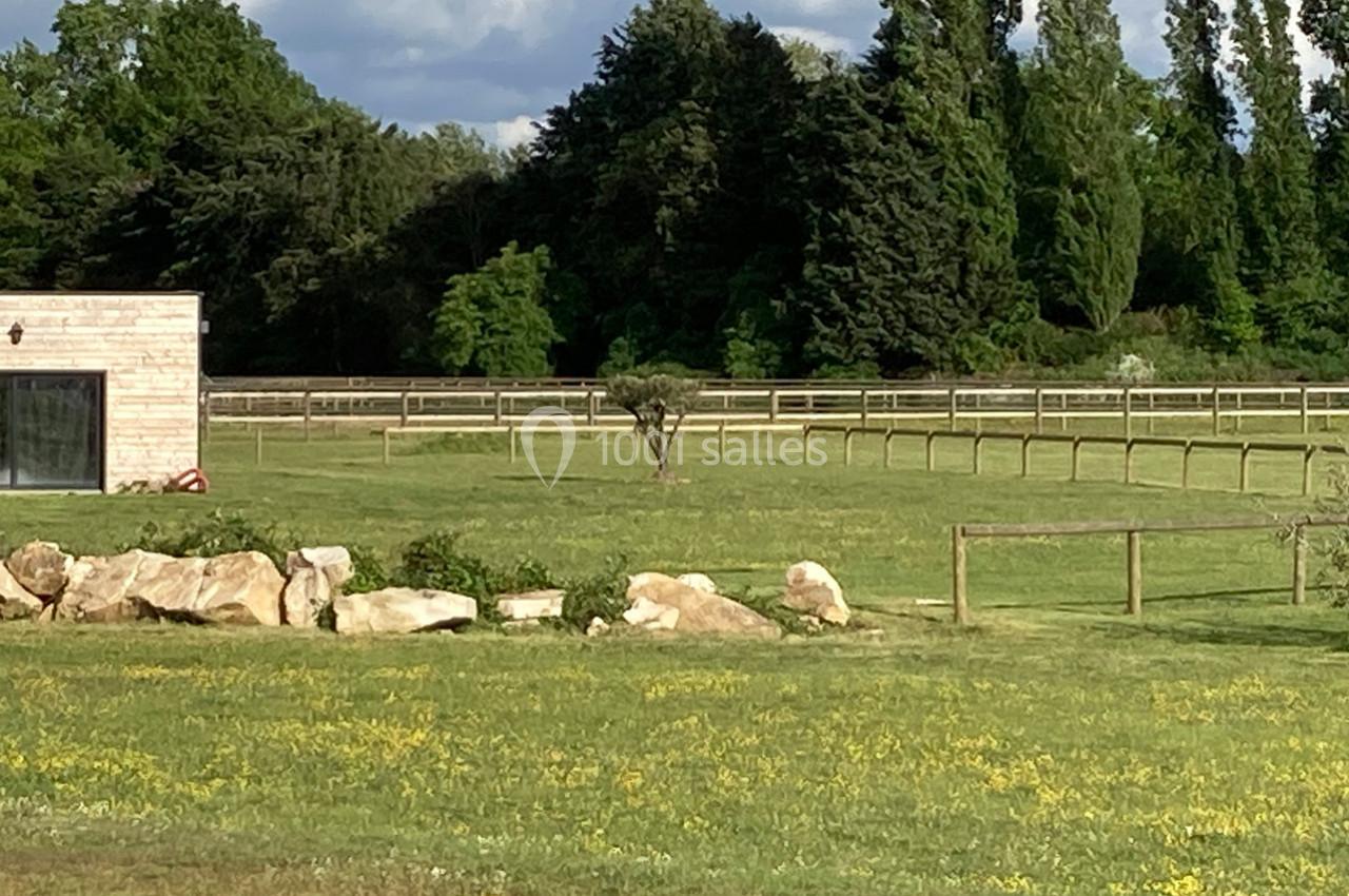 Un grand espace vert avec une clôture en bois, des arbres en arrière-plan et un bâtiment moderne à gauche.
