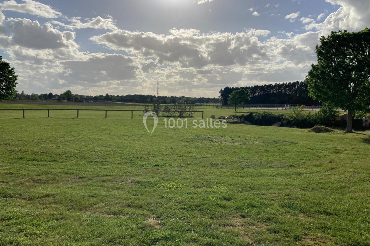Prairie verdoyante sous un ciel partiellement nuageux, bordée d'arbres et d'une clôture en bois.