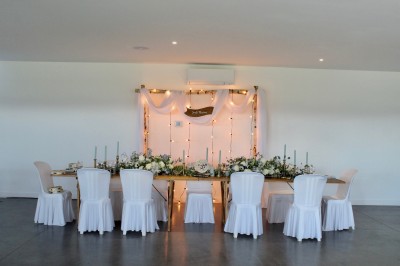 Salle de réception décorée avec des tables alignées, nappes blanches, chaises en bois et centre de table floral.