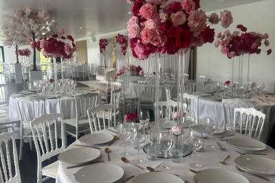 Salle de réception décorée avec des tables alignées, nappes blanches, chaises en bois et centre de table floral.