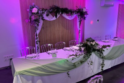 Salle de réception décorée avec des tables alignées, nappes blanches, chaises en bois et centre de table floral.