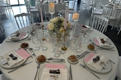 Salle de réception décorée avec des tables alignées, nappes blanches, chaises en bois et centre de table floral.