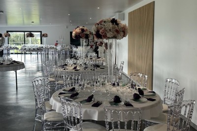 Salle de réception décorée avec des tables alignées, nappes blanches, chaises en bois et centre de table floral.