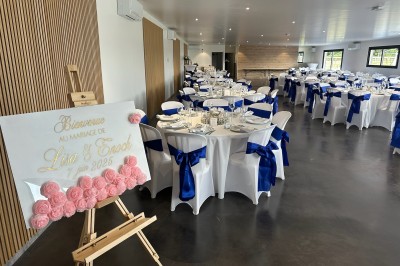 Salle de réception décorée avec des tables alignées, nappes blanches, chaises en bois et centre de table floral.